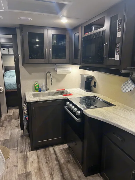 Modern RV rental interior: well-equipped kitchen with stove, microwave, sink, and a comfortable adjacent bedroom area.. Grand Design Transcend Xplor 2022