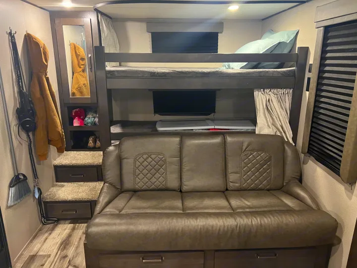 RV rental interior: cozy bunk beds over a couch, storage stairs, and compact living space with a mirror.. Grand Design Transcend Xplor 2022