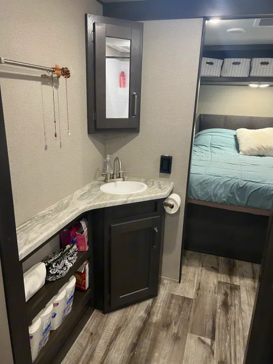 RV rental: Modern interior with a compact bathroom vanity, open storage, and a bedroom visible on wood-look flooring.. Grand Design Transcend Xplor 2022