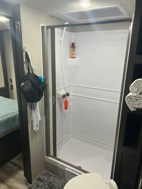 An RV rental interior showing a clean, compact bathroom with a white shower stall, toilet, and convenient storage.. Grand Design Transcend Xplor 2022