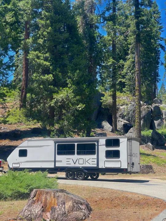 Evoke RV rental ready for camping in a sunny forest, surrounded by tall pines and rocks.. Travel Lite Evoke 2020