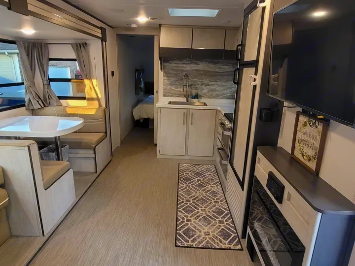 Modern RV rental interior: Dinette, well-equipped kitchen with sink, living area with TV/fireplace, and cozy bedroom beyond.. Travel Lite Evoke 2020