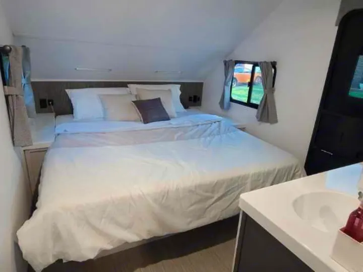 Cozy RV rental bedroom featuring a comfortable bed, window views, and a small vanity sink for convenience.. Travel Lite Evoke 2020
