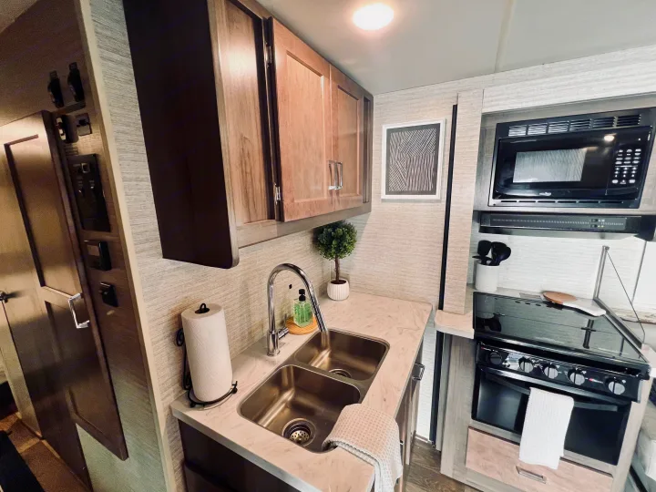 Modern RV rental kitchen with double sink, microwave, and stove, perfect for a cozy trip.. Winnebago Minnie Winnie 2022