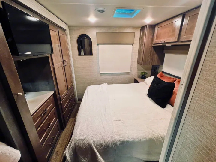 Inside an RV rental bedroom: cozy bed, flat-screen TV, modern cabinets, and a unique arched mirror.. Winnebago Minnie Winnie 2022