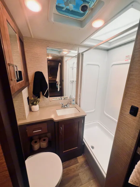 A bright, compact RV rental bathroom featuring a shower, toilet, and vanity with a sink. Ideal for travel.. Winnebago Minnie Winnie 2022