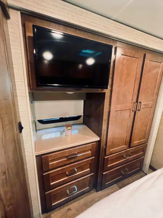 Inside an RV rental: a compact bedroom unit with a TV, countertop, drawers, and a built-in wardrobe for storage.. Winnebago Minnie Winnie 2022