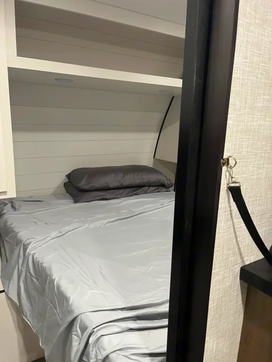RV rental interior: A compact bunk bed with light gray sheets, pillows, and a built-in shelf for comfort.. Jayco JayFlight SLX 2024