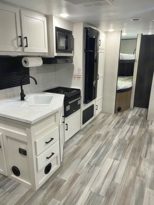Step inside this modern RV rental! Features a well-equipped kitchen with white cabinets, black appliances, and a cozy bunk bed area.. Jayco JayFlight SLX 2024