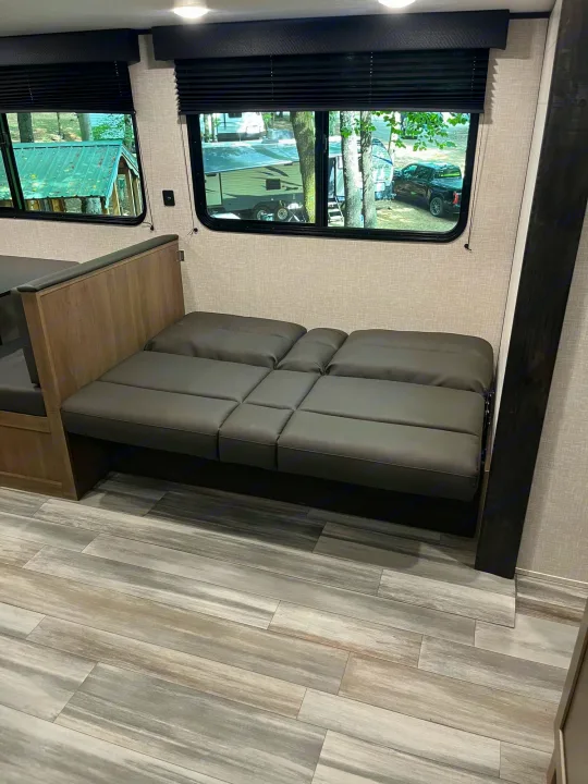 RV rental interior: laid-flat convertible sofa bed, large windows with campground view, and wood-look laminate flooring.. Jayco JayFlight SLX 2024