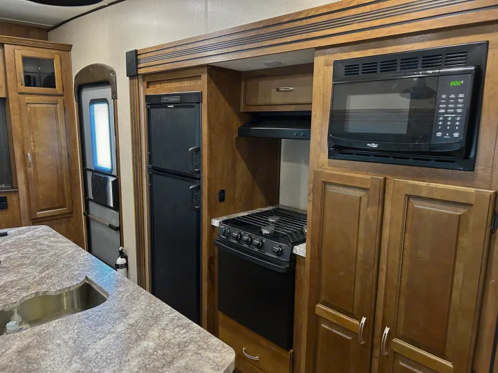 Well-equipped rv rental kitchen featuring a microwave, stove, large refrigerator, sink, and wood cabinetry.. Forest River Coachmen Chaparral Lite 2019