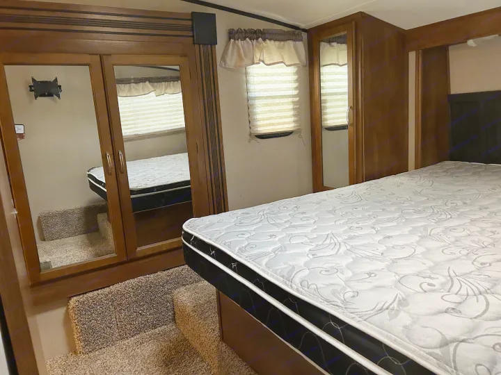RV rental bedroom with plush mattress, mirrored closet doors, and carpeted steps. Experience comfort on the road.. Forest River Coachmen Chaparral Lite 2019