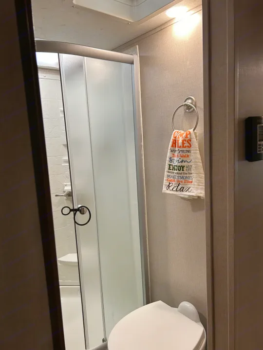 Compact RV rental bathroom with shower, toilet, and a "Camp Rules" towel.. Forest River Coachmen Chaparral Lite 2019