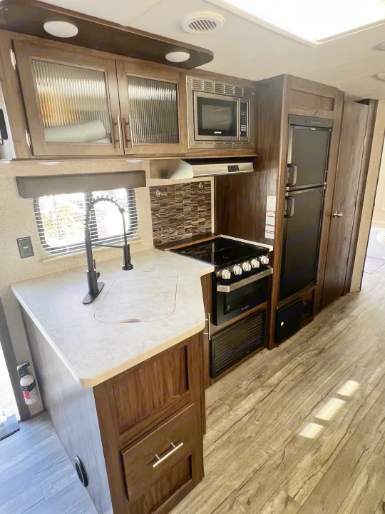 Explore this clean, modern RV rental kitchen, complete with a sink, stove, microwave, and refrigerator, ready for your travels.. Forest River Cherokee Grey Wolf 2019