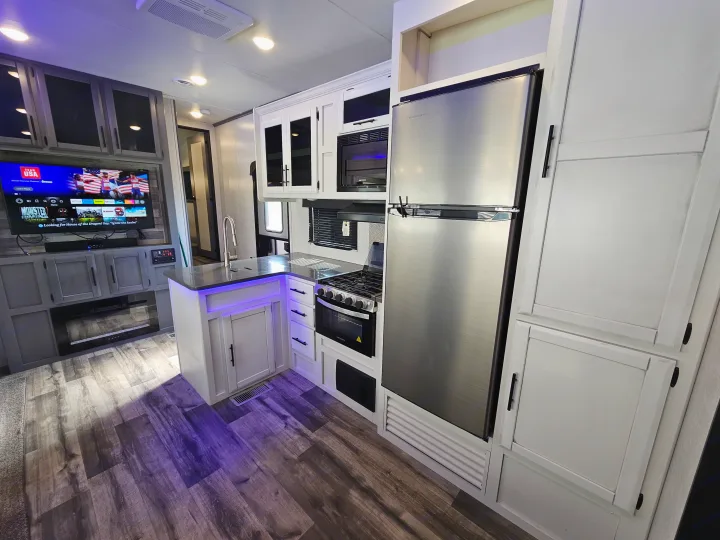 Modern RV rental interior with a full kitchen, stainless steel appliances, and a living area with an entertainment center and TV.. Crossroads Volante 2023