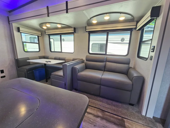 Interior of a comfortable RV rental, showcasing a dark gray sofa, U-shaped dinette with table, and multiple windows.. Crossroads Volante 2023