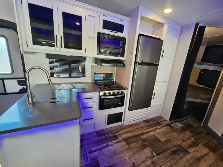 Modern rv rental kitchen with stainless steel appliances (microwave, stove, fridge), a sink, and bunk beds.. Crossroads Volante 2023
