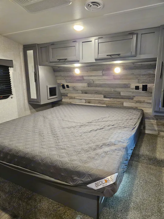 RV rental interior: a sleek grey bedroom with a quilted bed, wooden headboard, ample storage, and bedside charging points.. Crossroads Volante 2023