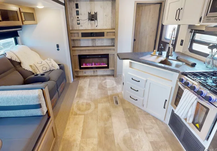 Inside a modern RV rental: cozy living space with sofa & fireplace, integrated kitchen with sink & stove.. Forest River Puma 2023