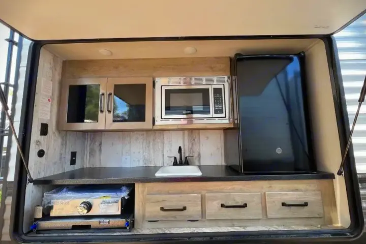 Full outdoor kitchen on this RV rental: microwave, sink, fridge, and pull-out cooktop, ideal for camping adventures.. Forest River Puma 2023