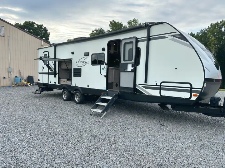 A white Spirit Ultra-Lite travel trailer/RV with an open outdoor kitchen and steps on a gravel lot. Ideal for your next rv rental.. Coachmen 2021 Coachman Sprinter Campfire Edition 2021