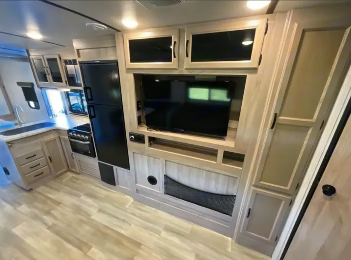 Inside an RV rental: a light-toned kitchen with sink, stove, fridge, and an entertainment center featuring a TV.. Coachmen 2021 Coachman Sprinter Campfire Edition 2021