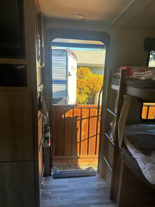 Welcome to your rv rental! Interior view of open door, bunk beds & storage. Another trailer & autumn foliage visible outside.. Grand Design Imagine 2020