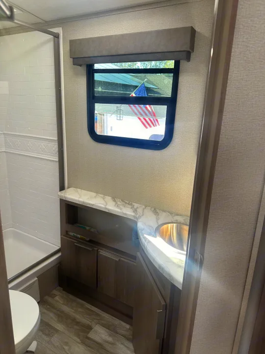 Clean RV rental bathroom featuring a shower, toilet, and vanity with a sink and window.. Grand Design Imagine 2020