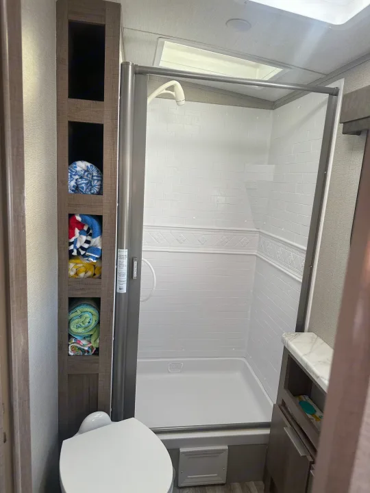 This modern RV rental bathroom features a spacious shower, compact toilet, and handy built-in towel shelves.. Grand Design Imagine 2020