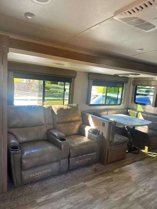 RV rental's inviting interior: comfy recliners, U-shaped dinette, and bright windows define this travel home.. Grand Design Imagine 2020