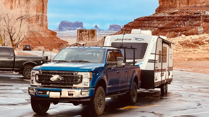 A blue Ford Super Duty pickup tows a Jayco RV rental through a snow-dusted desert landscape with iconic red rock mesas.. Jayco White Hawk 2018