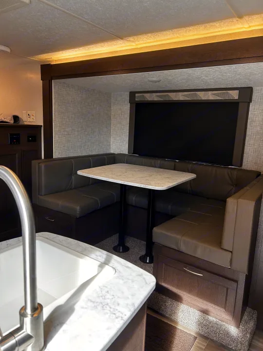 RV rental interior showcasing a U-shaped dinette with a marble table, dark cushioned seating, and a kitchen sink view.. Forest River Wildwood Cruise Lite 2019
