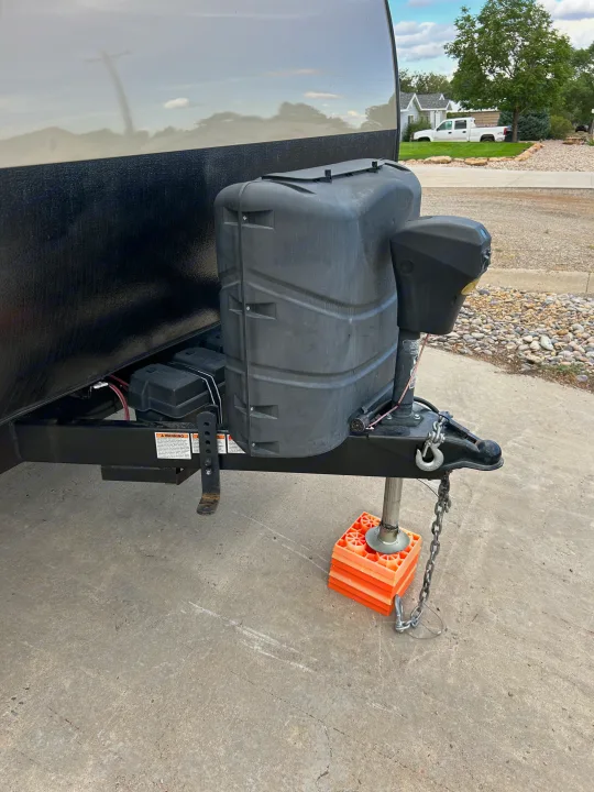 Front of an **RV rental** showing the electric tongue jack resting on orange leveling blocks, propane tanks, and batteries.. Forest River Wildwood Cruise Lite 2019