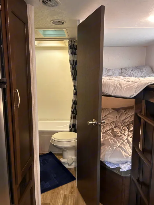Explore this RV rental's clever layout: a full bathroom on the left, complete with toilet and shower, and cozy bunk beds on the right.. Forest River Wildwood Cruise Lite 2019