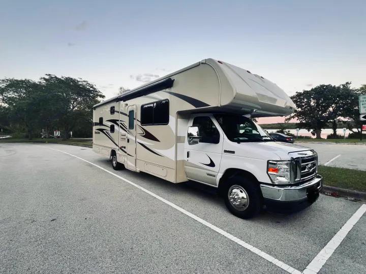 Spacious beige & white RV rental, perfect for outdoor travel, parked by a lake at dusk.. Winnebago Minnie Winnie 2022