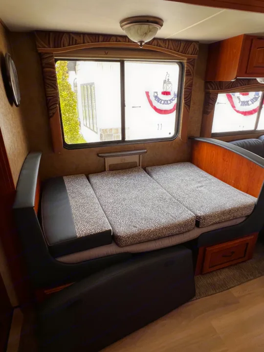 Inside an rv rental: patterned convertible bed/dinette near windows with patriotic buntings, wood trim & storage.. Forest River Coachmen Mirada 32 DSF 2011
