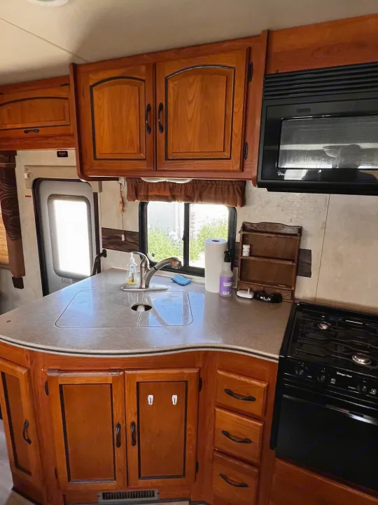 RV rental kitchen: Features include warm wood cabinets, a sink, microwave, and stove, providing home comforts.. Forest River Coachmen Mirada 32 DSF 2011