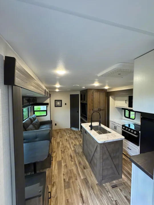 rv rental: Bright interior featuring a modern kitchen island with sink, a comfortable sofa, and wood-look flooring. Perfect for mobile adventures.. Venture RV 327VIK 2024