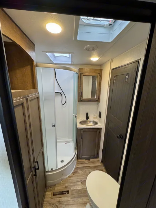 Compact RV rental bathroom with shower, sink, toilet, and storage cabinets, efficiently designed for travel.. Venture RV 327VIK 2024