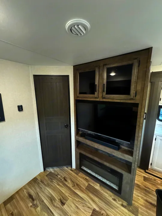 RV rental interior with a view of the entertainment center featuring a TV, electric fireplace, and wood-look flooring.. Venture RV 327VIK 2024