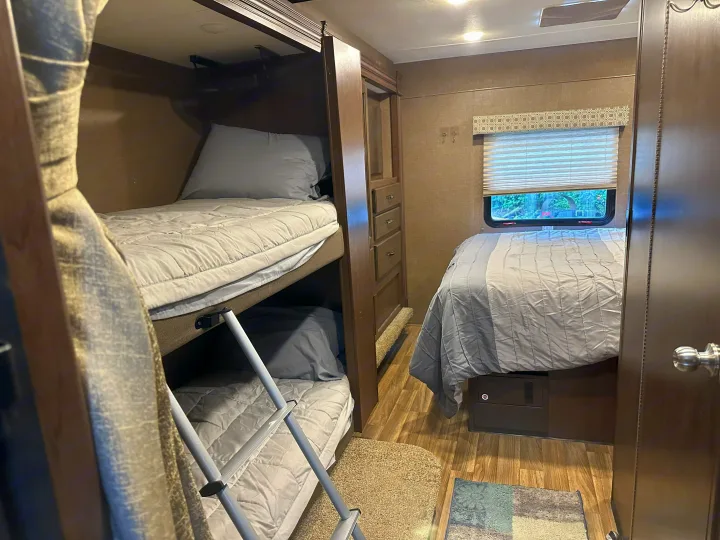 Cozy RV rental bedroom featuring bunk beds, a main bed, and storage cabinetry. Ideal for family adventures.. Thor Four Winds 2019