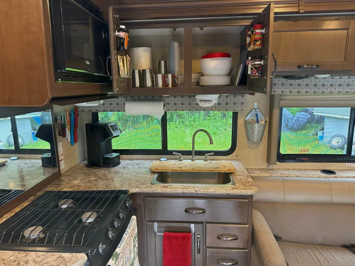Bright RV rental kitchen view: microwave, stove, sink, and organized cabinets, perfect for travelers.. Thor Four Winds 2019