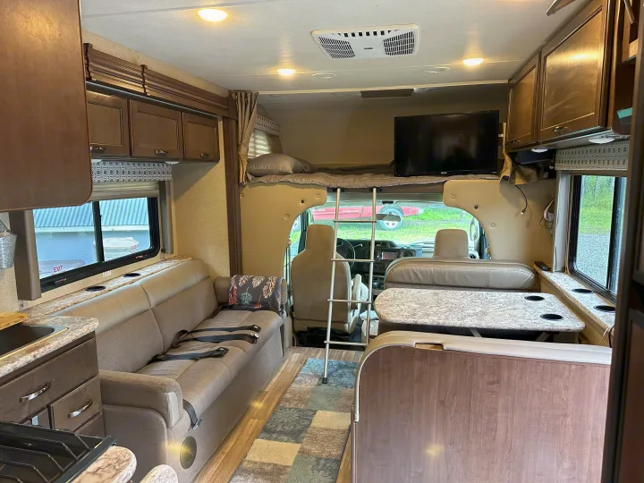 Well-lit RV rental interior with kitchen, dinette, sofa, and over-cab bunk bed, ideal for road trips.. Thor Four Winds 2019