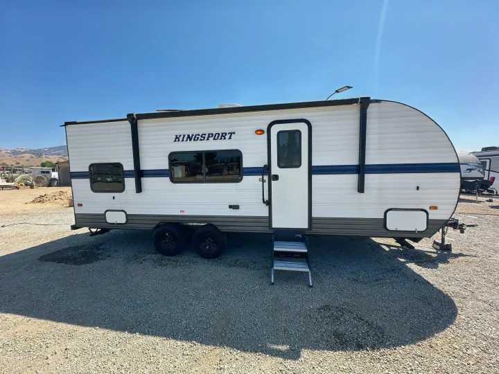 A new white Kingsport travel trailer RV, with steps deployed, sits ready for an RV rental adventure on a gravel lot.. Gulf Stream Kingsport 2022