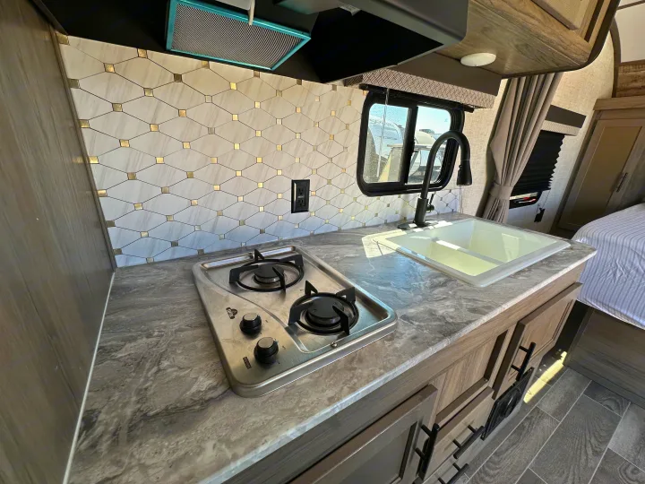 RV rental kitchen showcasing a modern two-burner stove, white sink, and stylish backsplash over a gray counter.. Gulf Stream Kingsport 2022