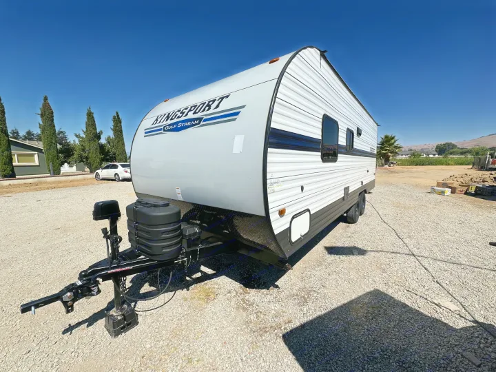 A white Kingsport Gulf Stream travel trailer on a gravel lot under a clear blue sky. Perfect for an RV rental.. Gulf Stream Kingsport 2022