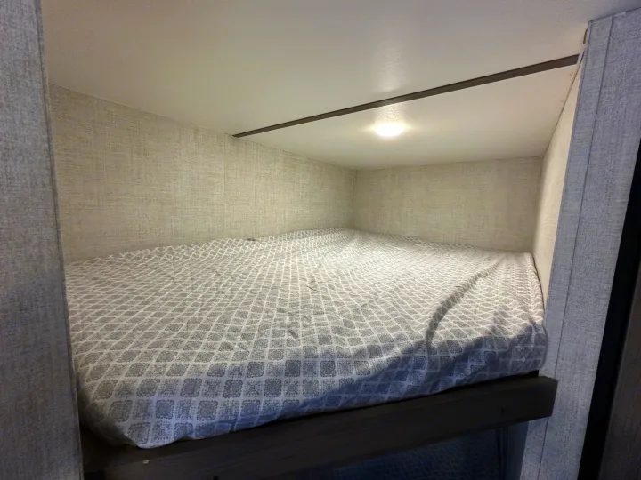 RV rental bunk bed interior with patterned sheets and overhead light, ideal for compact sleeping in a mobile home.. Gulf Stream Kingsport 2022