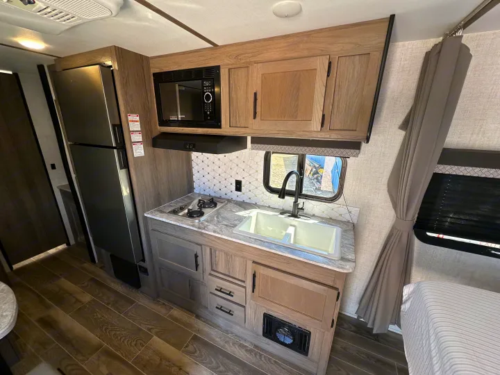 This rv rental features a modern, compact kitchen with a refrigerator, microwave, stove, sink, and ample cabinet storage.. Gulf Stream Kingsport 2022