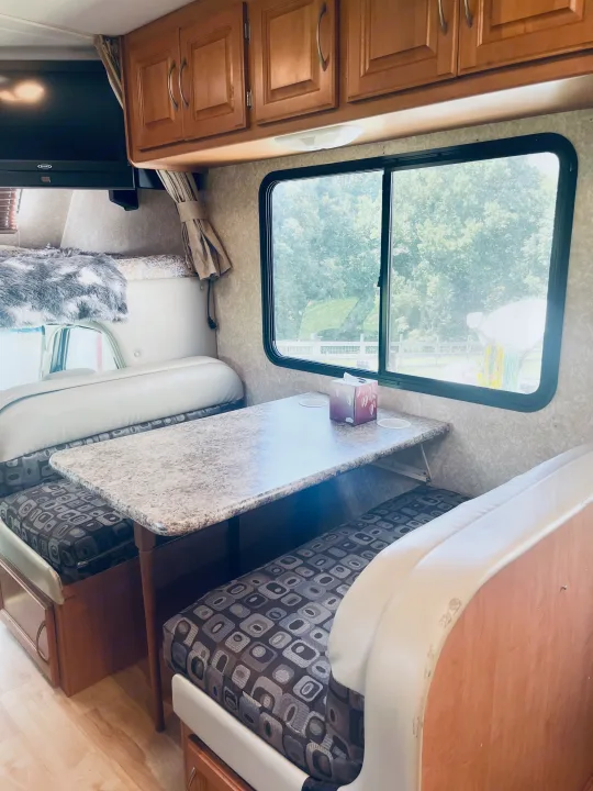 Cozy RV rental interior showing a dinette with patterned seating, wood cabinets, and a large window view.. Four Winds Chateau 2011