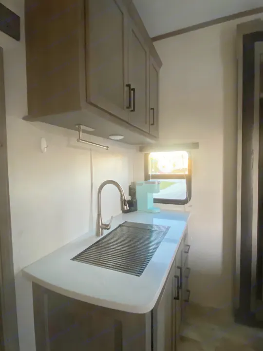 Inside an RV rental: a well-equipped kitchen with a large sink, drying rack, coffee maker, and sleek cabinets.. Keystone Carbon 2020